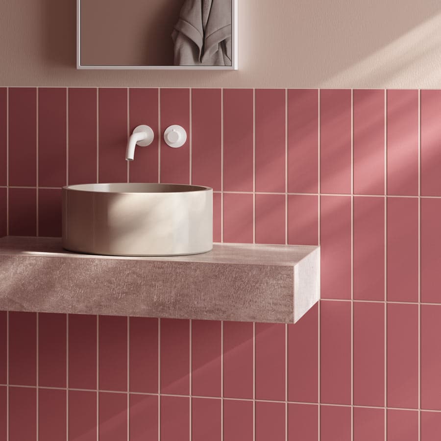 Modern bathroom with pink tiled wall, round beige sink on a floating countertop, and a white faucet. Soft lighting creates gentle shadows.