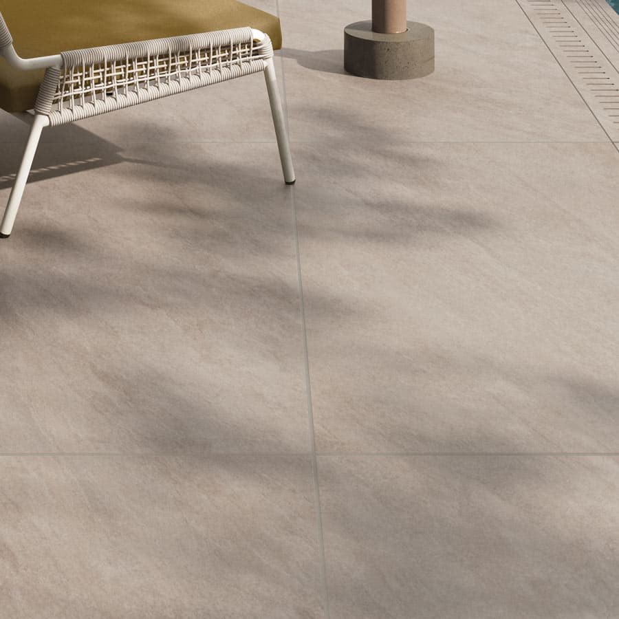 A sunlit patio with beige tiles, featuring a modern chair with a woven backrest and a glimpse of a pool edge. Shadows create a serene ambiance.